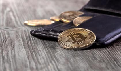 Portefeuille en cuir noir contenant plusieurs pièces physiques de Bitcoin posées sur une table en bois.