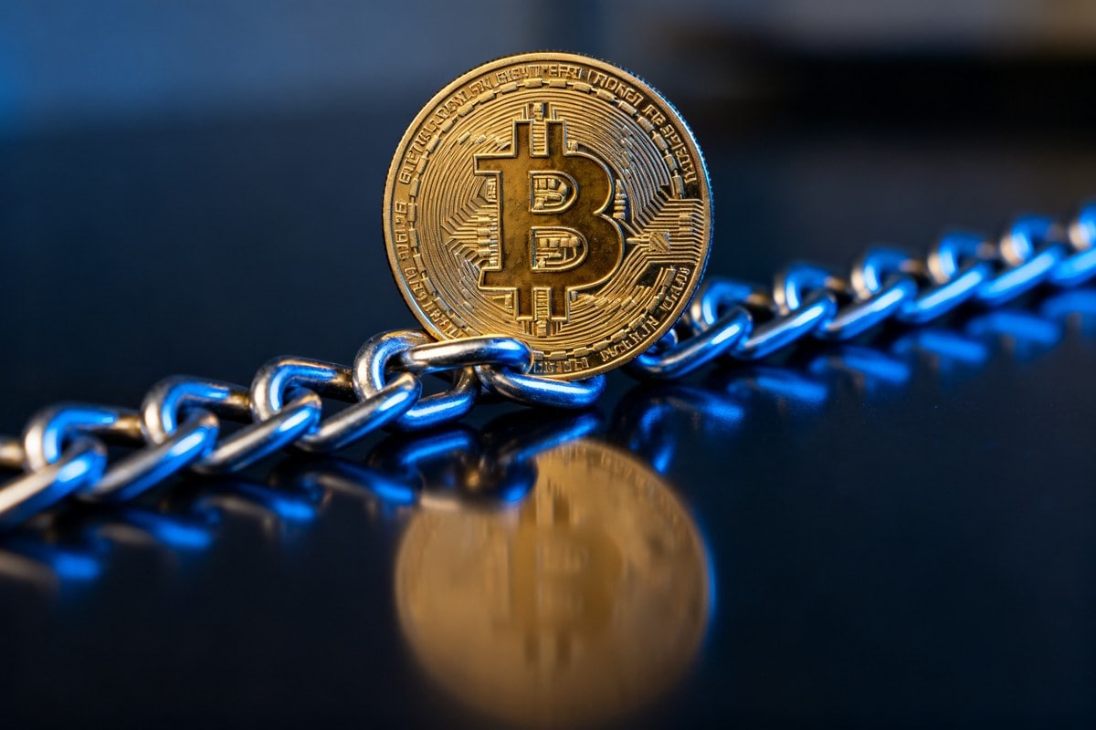 Pièce dorée Bitcoin posée sur une chaîne métallique sur fond sombre éclairé de bleu