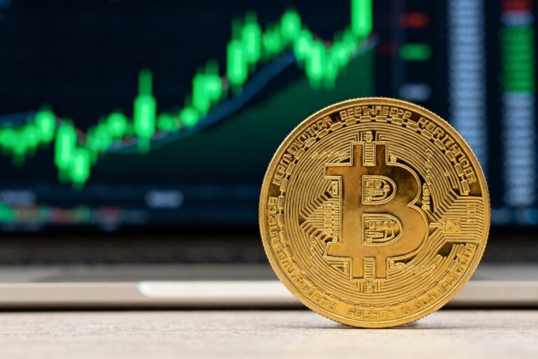 Pièce dorée de bitcoin devant un écran de cotation affichant des chandeliers en hausse