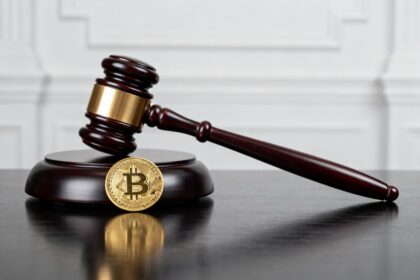Marteau de juge posé sur son socle à côté d'une pièce dorée de cryptomonnaie sur un bureau sombre