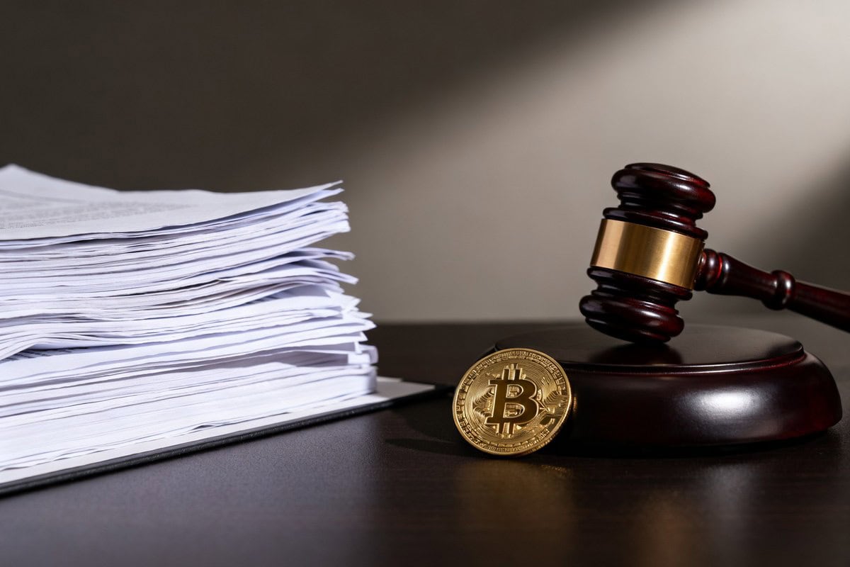 Un maillet de juge posé près d'une pile de documents et d'une pièce dorée au symbole du bitcoin.