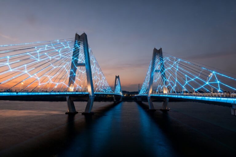 Deux ponts suspendus illuminés de lumières bleues reliés au-dessus de l'eau au crépuscule