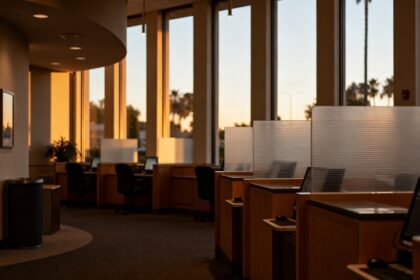 Intérieur désert d'une agence bancaire au crépuscule, guichets fermés derrière des cloisons vitrées
