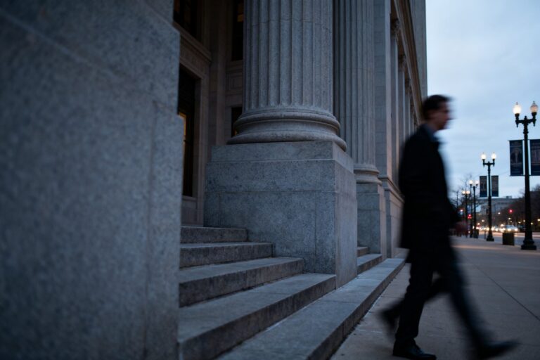 Colonnes et marches en pierre d'un palais de justice au crépuscule, un passant flou sur le trottoir
