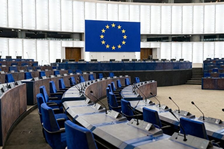 Hémicycle européen vide, sièges bleus et micros devant un panneau au cercle d'étoiles jaunes